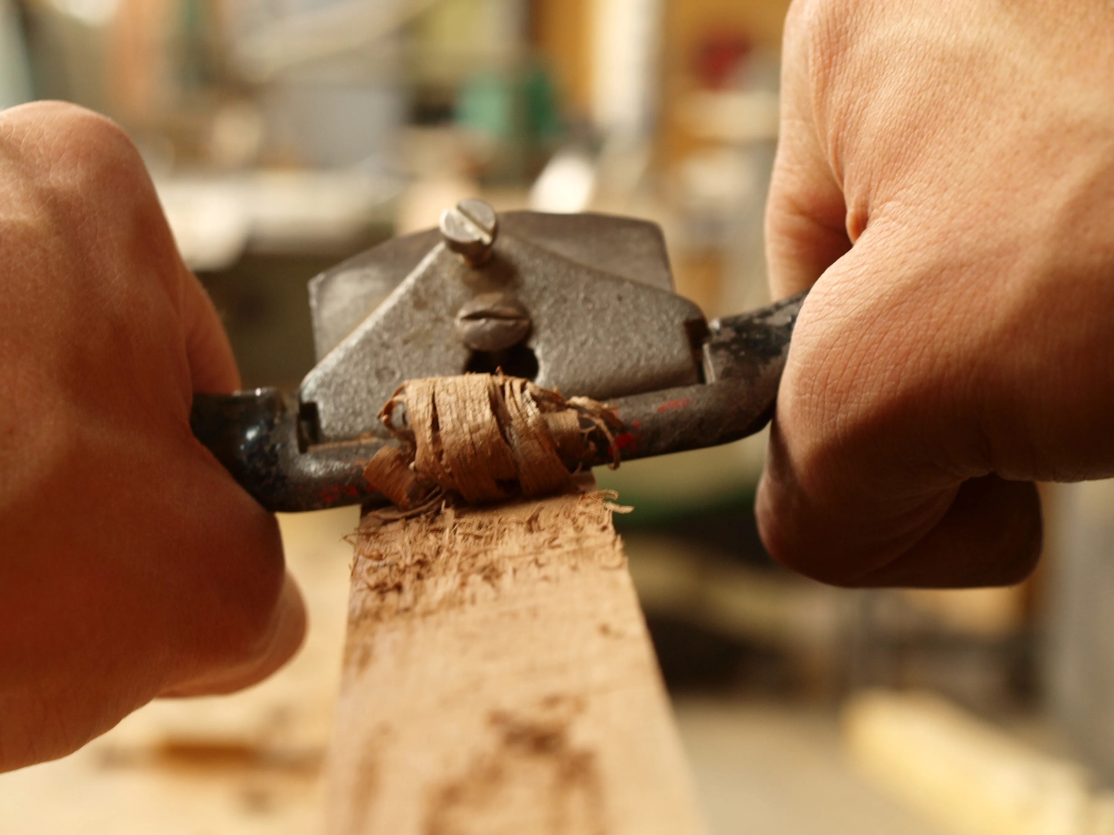 Nahaufnahme: Hände hobeln Holzlatte mit Handhobel in der Werkstatt